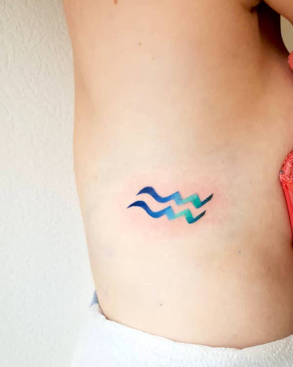 A rib tattoo of the Water-bearer symbol by @cora_linez