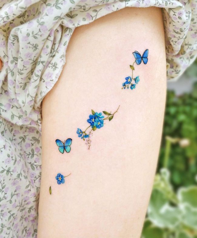 Small blue butterfly and flowers tattoo by @songe.tattoo