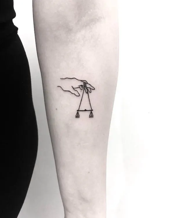 A tiny hand tattoo with a balance scale